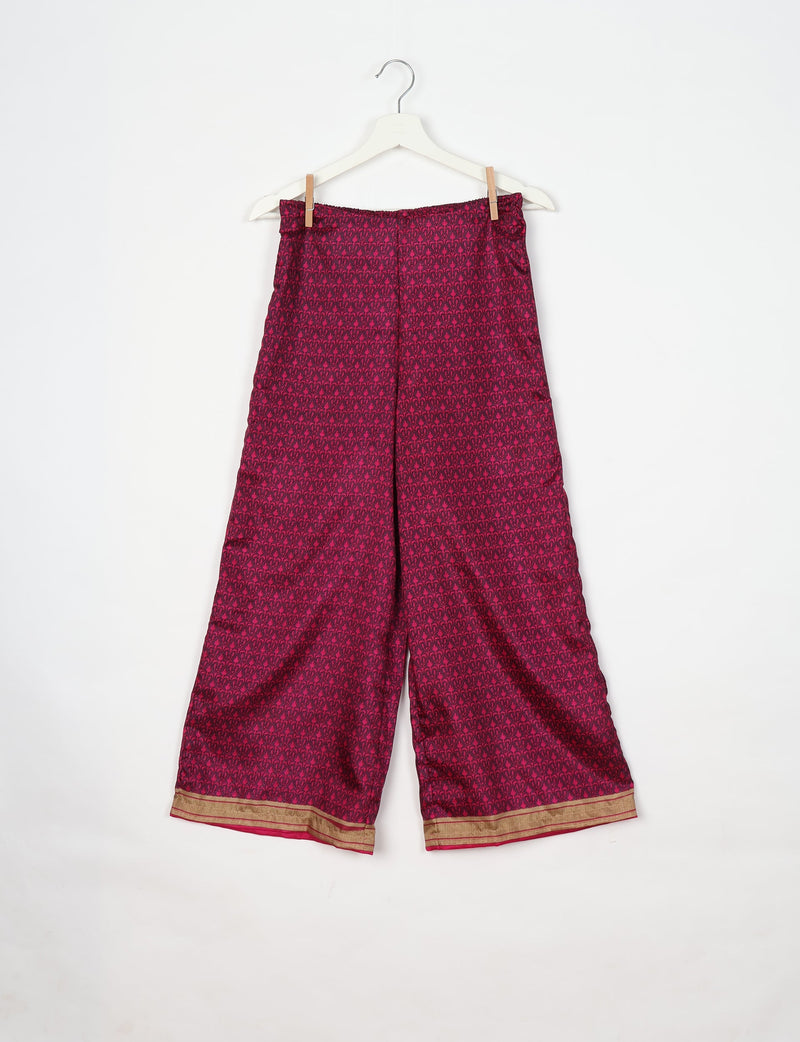 Pink tunic pants with dark micro floral pattern and gold border hem, hanging on white hanger against white background