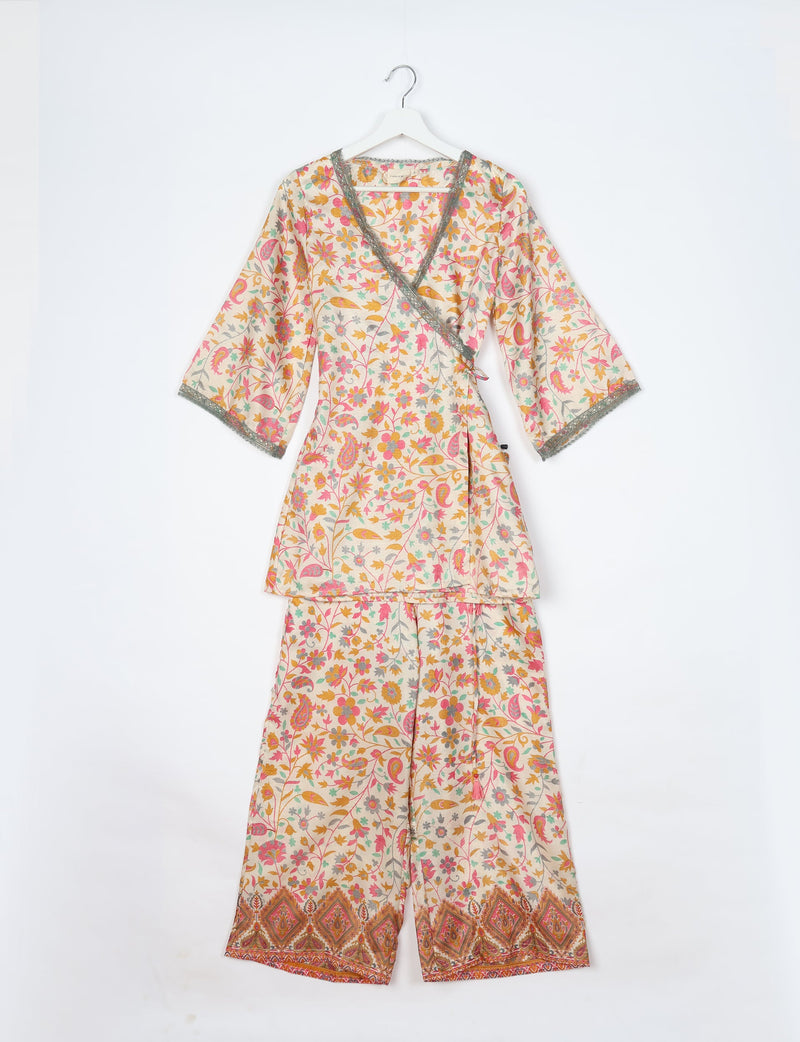 White tunic set with pink, yellow, and green floral tropical print, wrap-style top with lace trim, and matching pants with