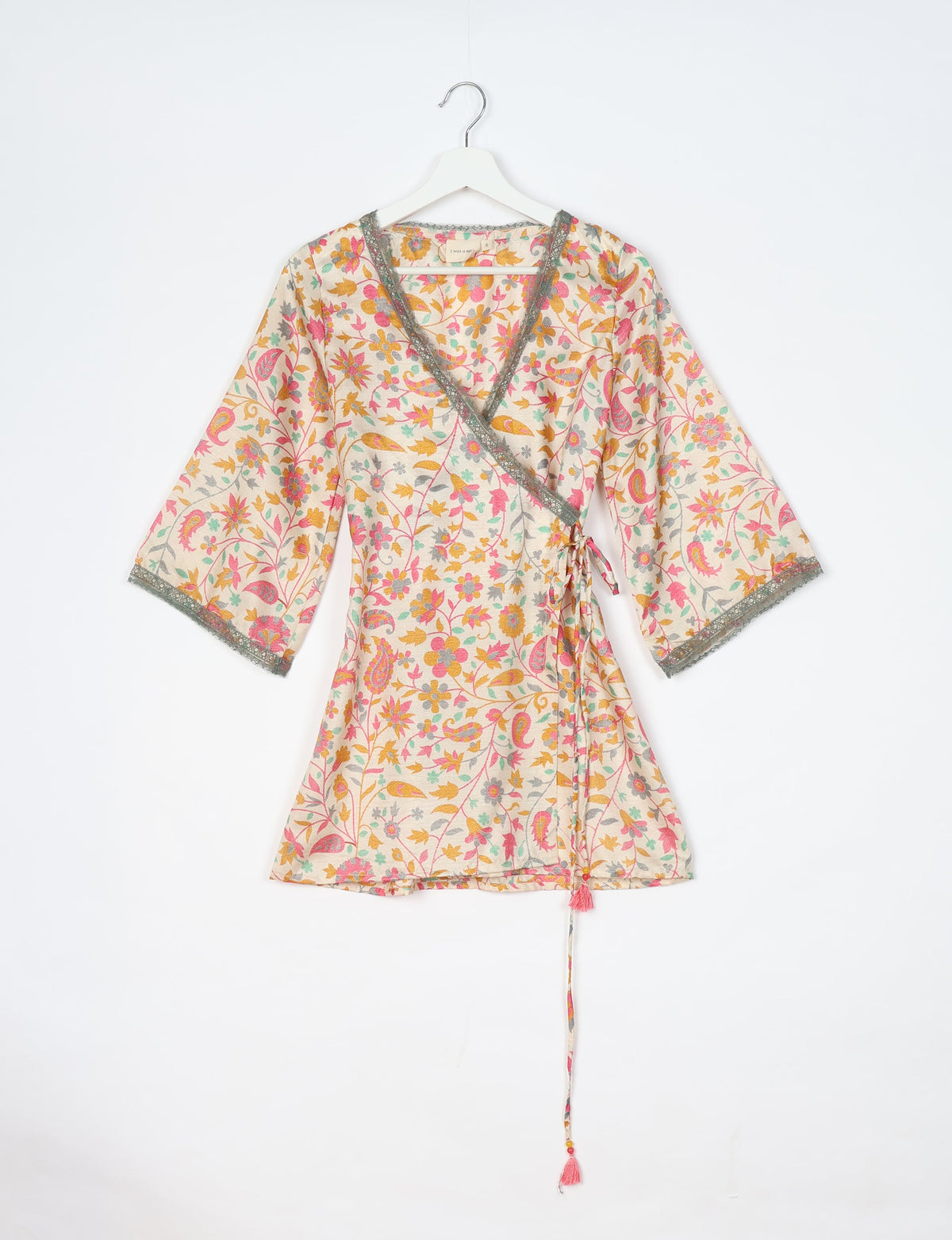 White tunic with pink, yellow, and green floral tropical print, V-neck, lace trim, and tie waist, hanging on white hanger