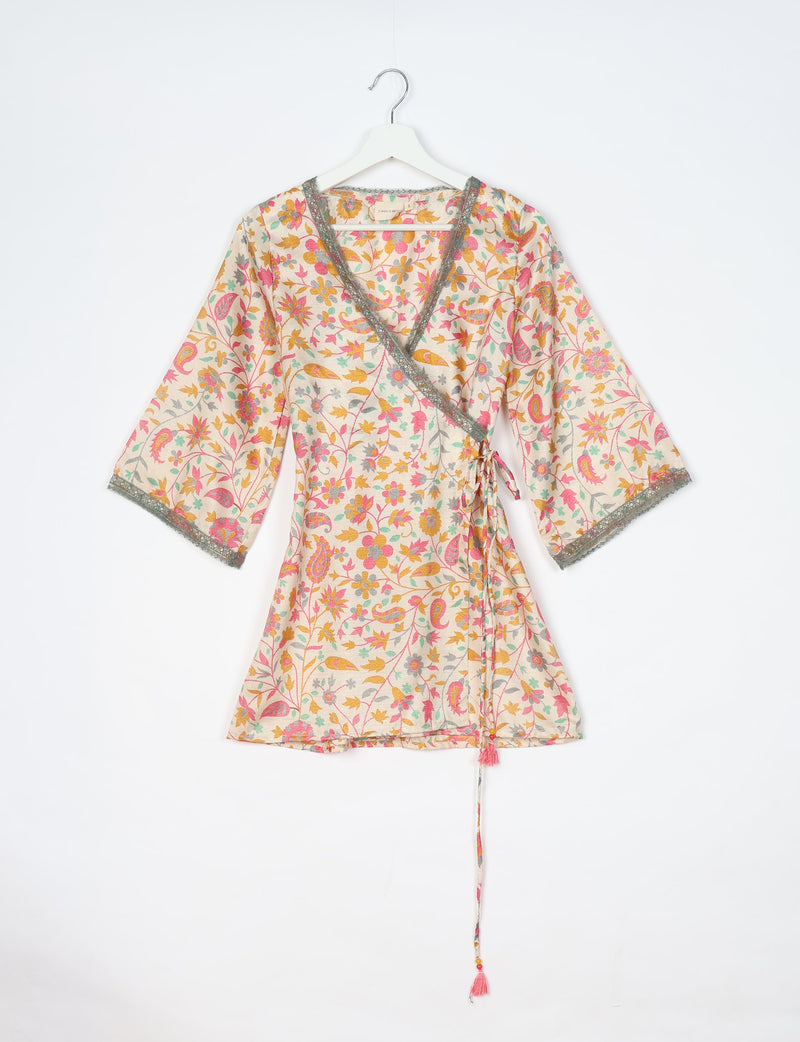 White tunic with pink, yellow, and green floral tropical print, V-neck, lace trim, and tie waist, hanging on white hanger