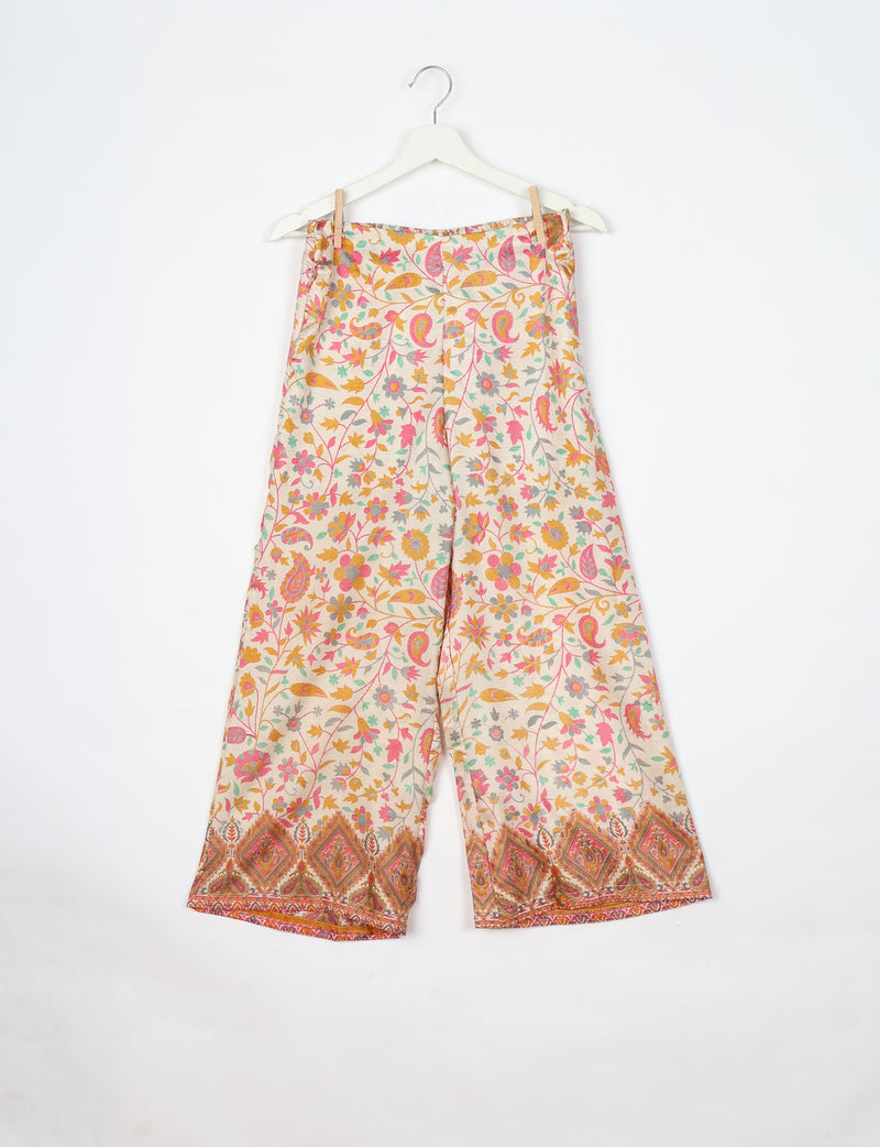 White fabric pants with pink, orange, and green floral and paisley print, wide leg, hanging on white hanger
