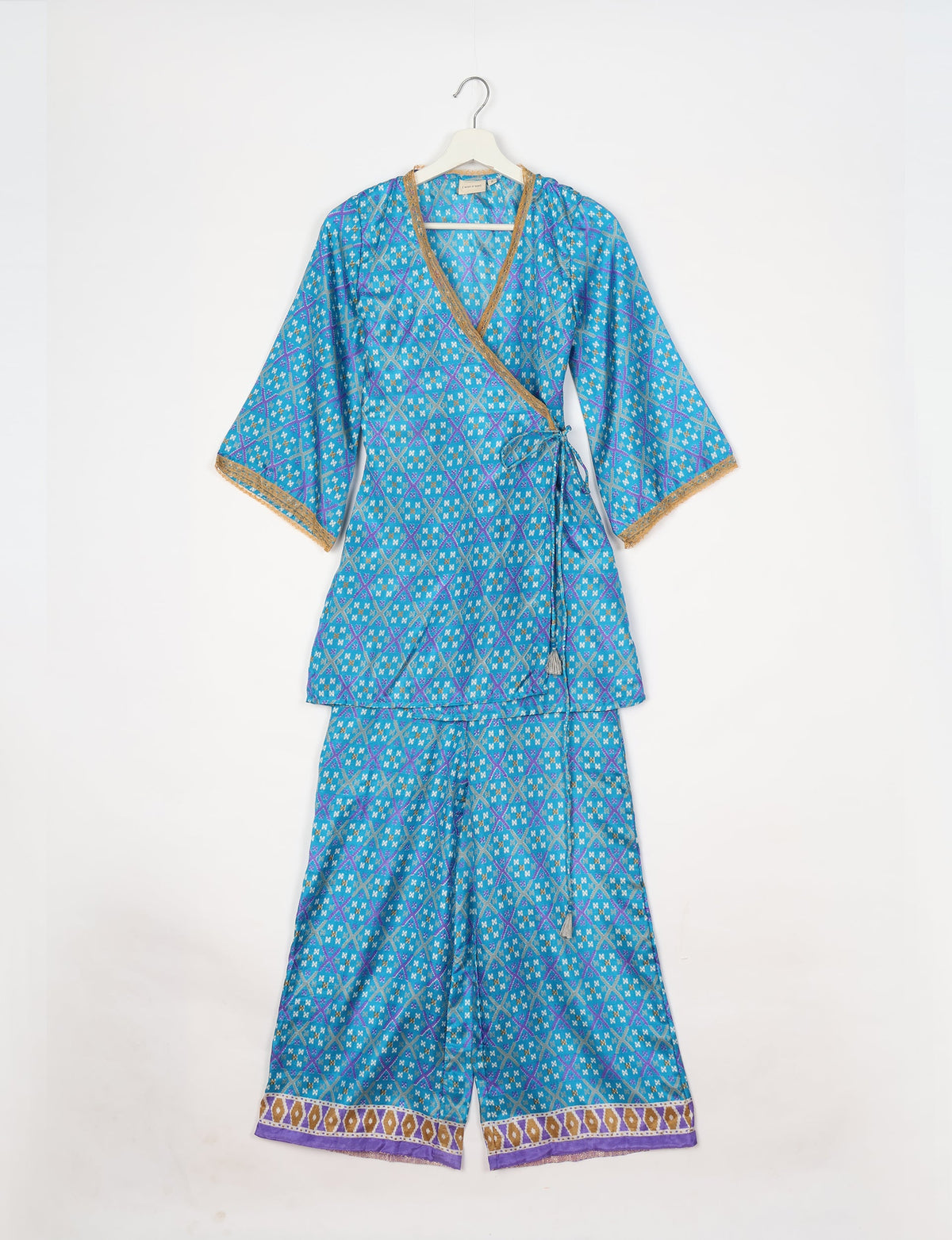 Blue geometric patterned tunic set with wrap top, gold trim on neckline and sleeves, and matching wide-leg pants with border hem