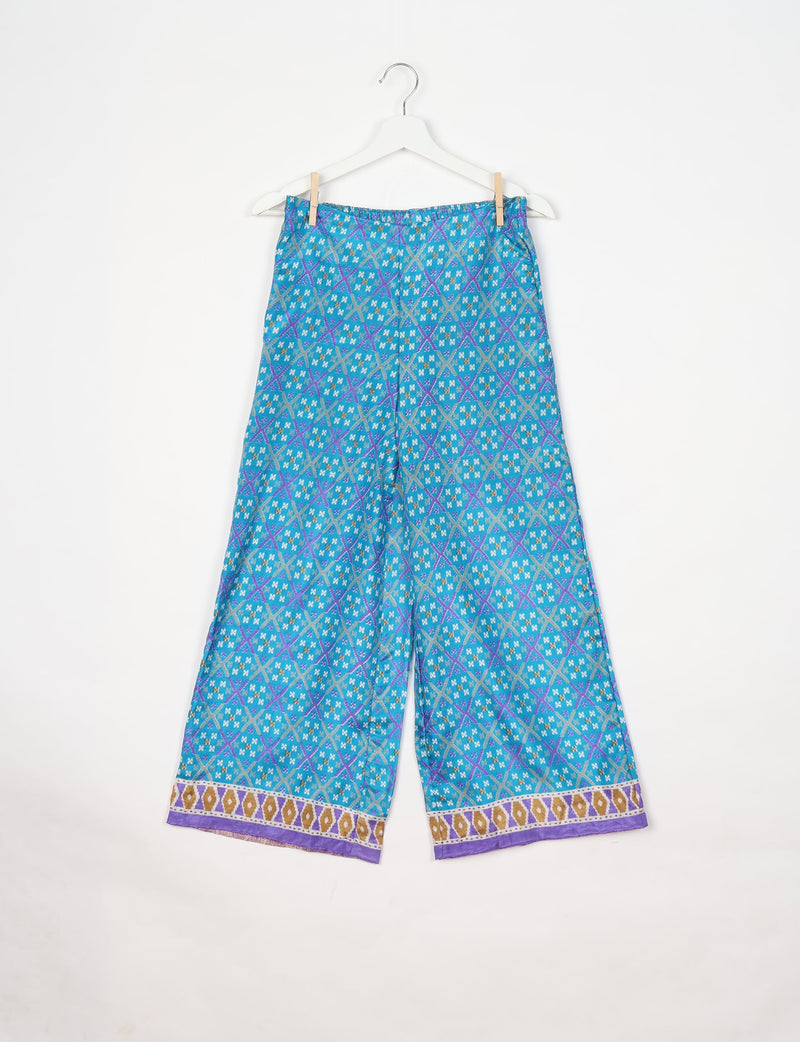 Blue geometric patterned wide-leg pants with elastic waistband and purple, gold, and white border detail, hanging on white hanger