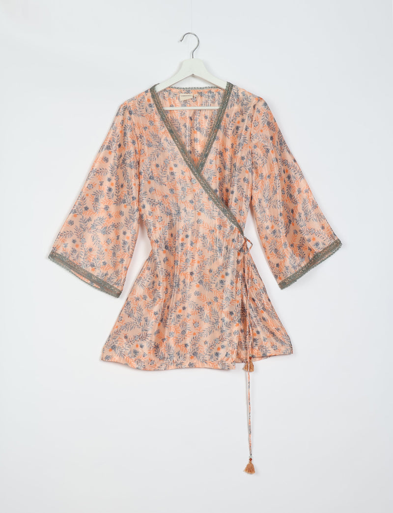 Pink floral wrap tunic with gray lace trim on neckline and sleeves, hanging on white hanger against white background