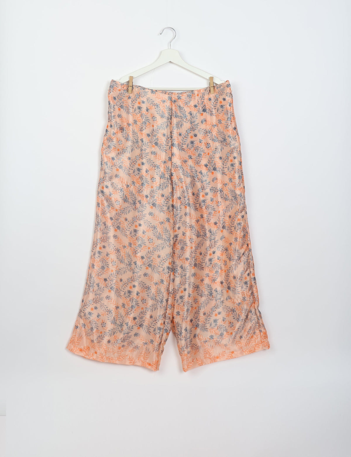 Pink and gray floral patterned wide-leg pants hanging on a white hanger against a white background