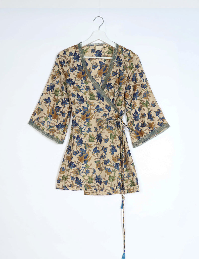 Beige wrap tunic with blue, green, and brown leaf print, lace trim on neckline and sleeves, hanging on white hanger