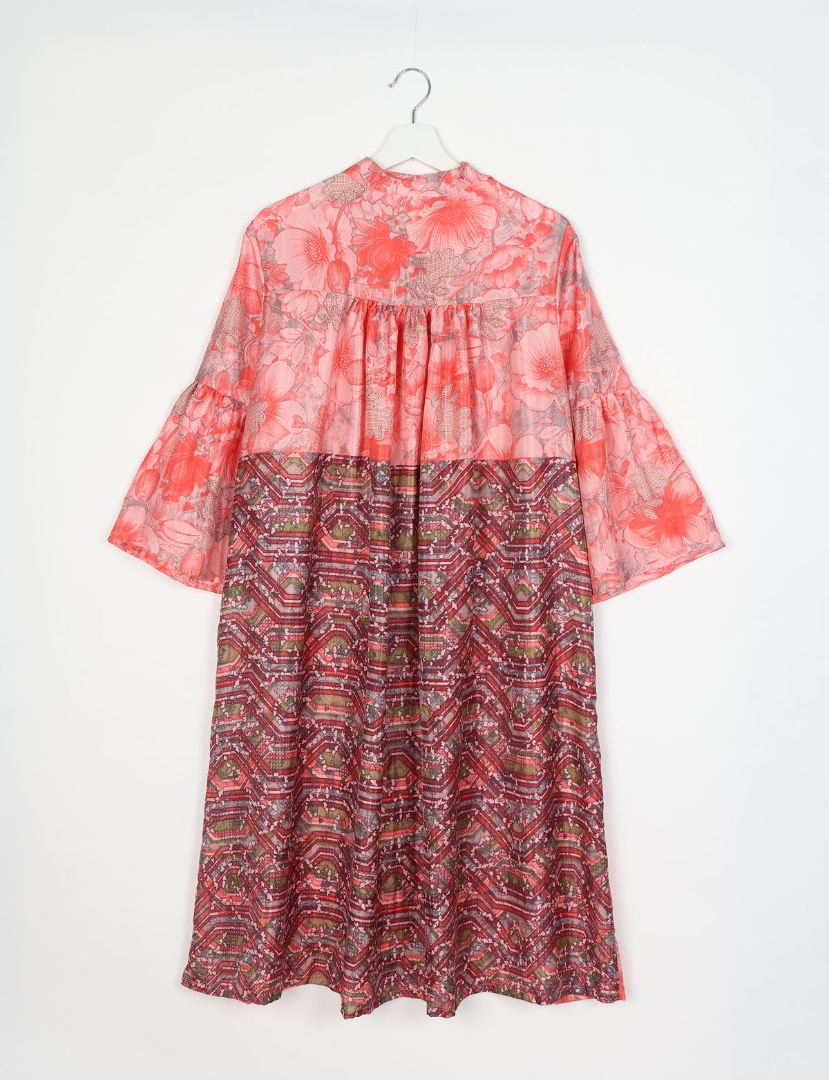 Pink floral bell sleeve coat with gathered back yoke and geometric patterned lower half, hanging on white hanger, back view