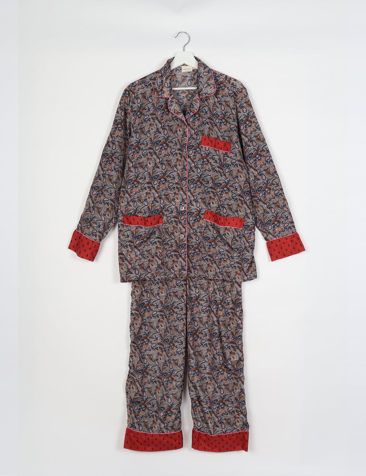 Long-sleeve grey tropical print pajama set with red cuffs, pocket trim, button front, and notched collar hanging on white hanger