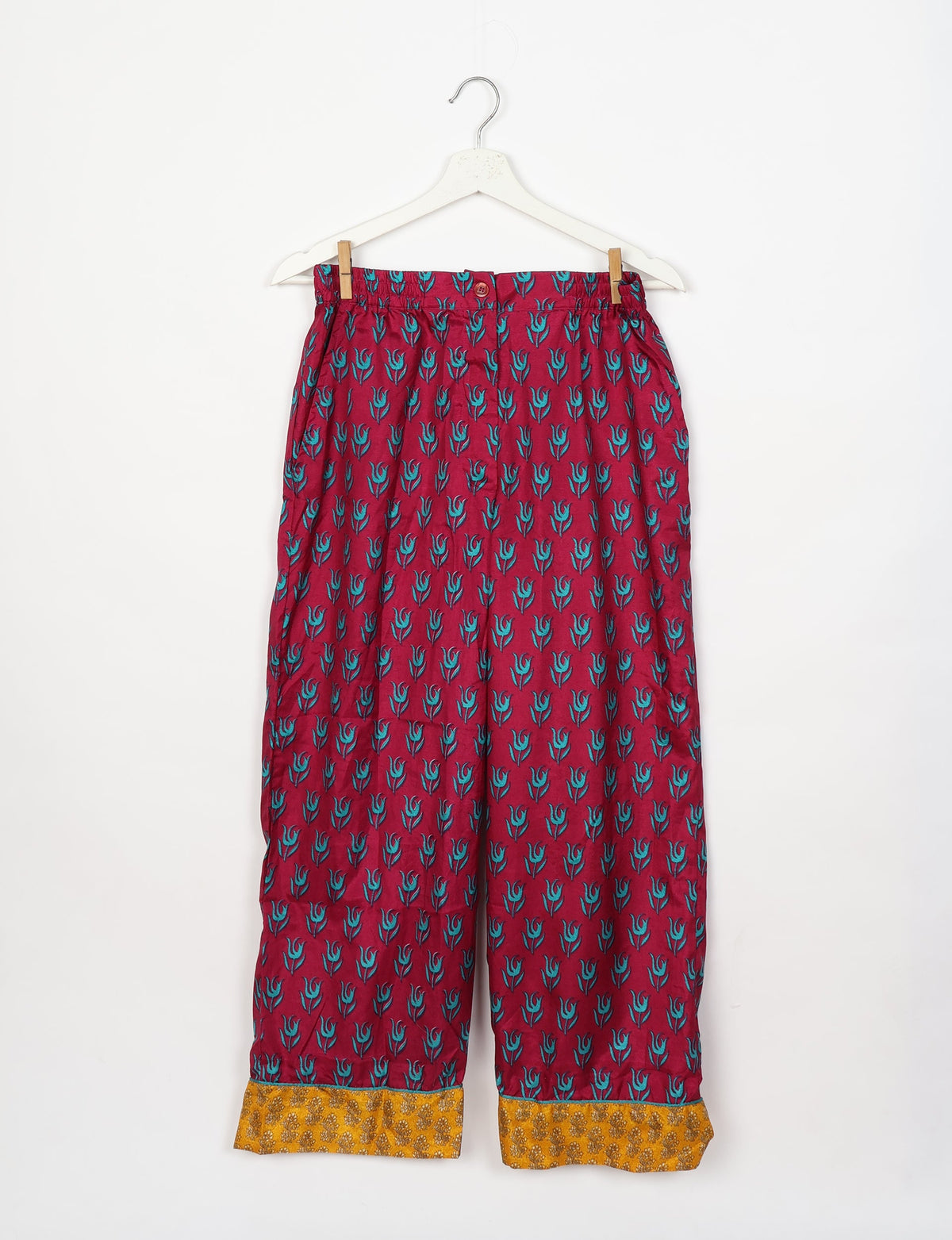 Red pajama pants with blue floral print and yellow patterned cuffs hanging on a white hanger against a white background