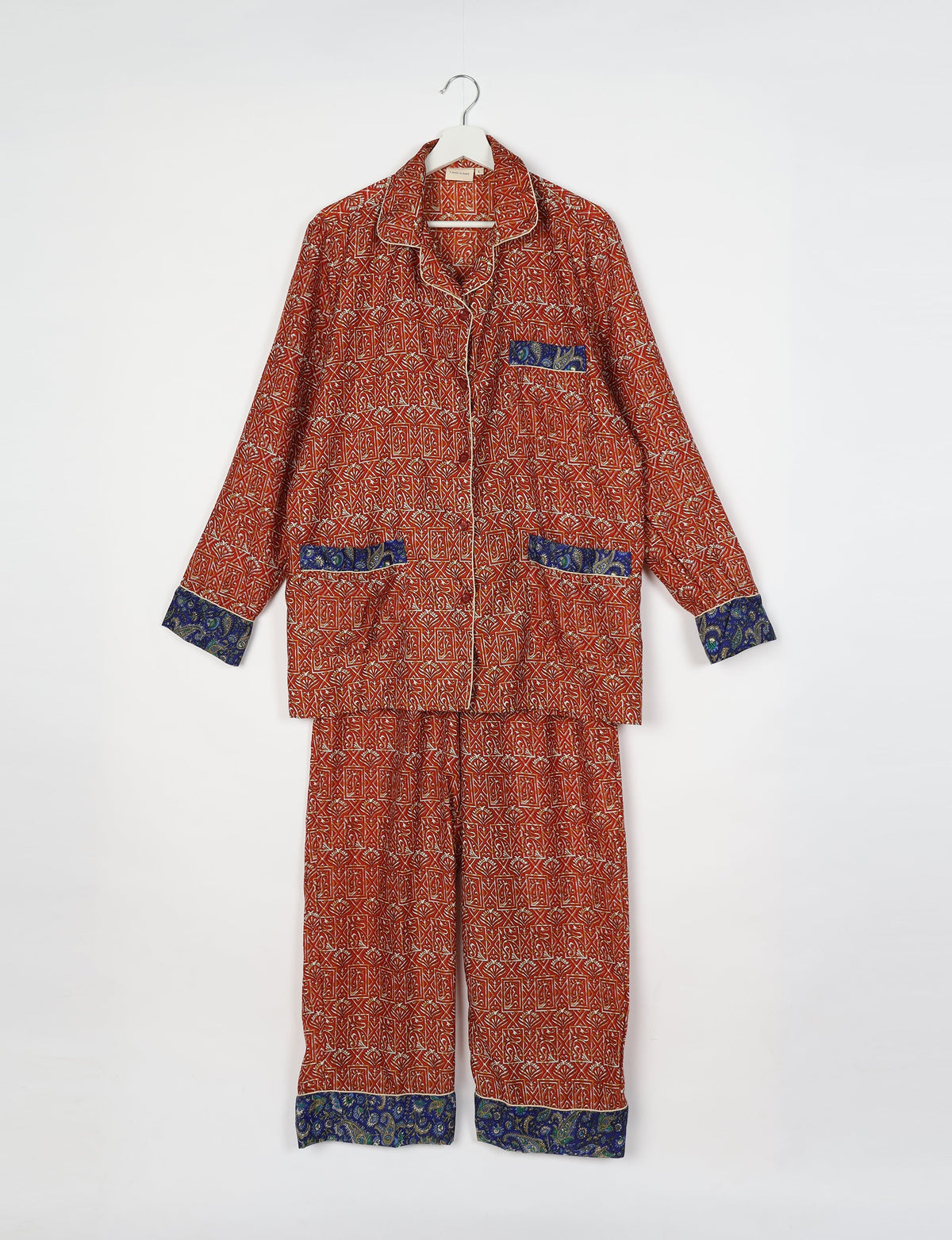 Long-sleeve pajama set with red geometric and floral print, blue paisley trim on cuffs, pockets, and pant hems, hanging flat