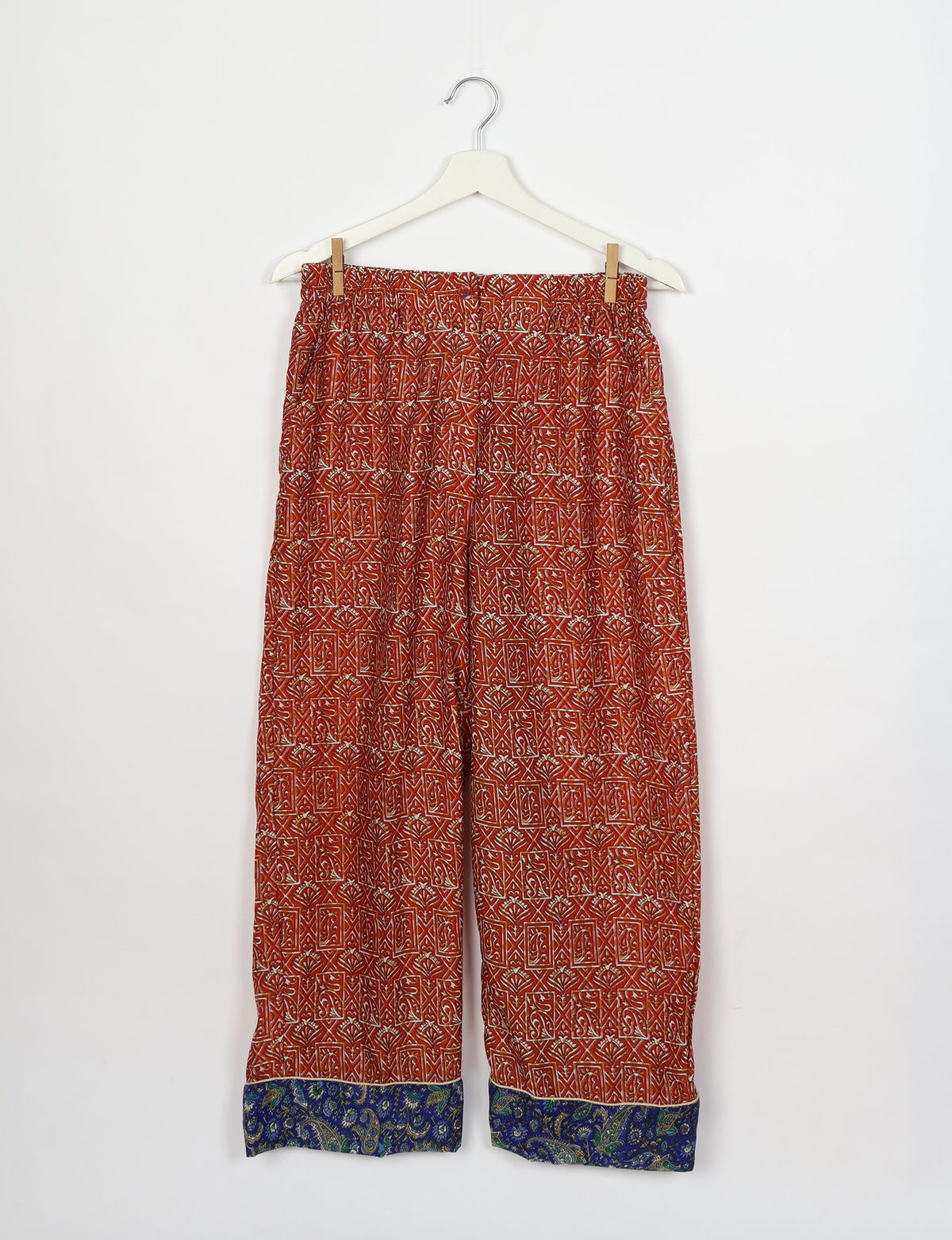 Red patterned pants with elastic waistband and blue paisley cuffs hanging on white hanger against white background