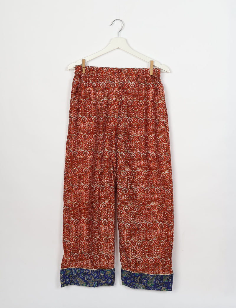 Red patterned pants with elastic waistband and blue paisley cuffs hanging on white hanger against white background