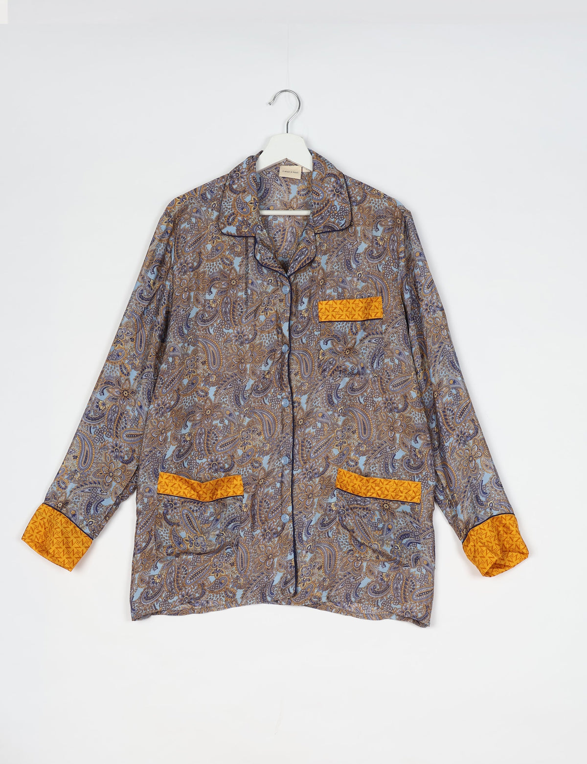 Long-sleeve pajama top with blue and brown paisley pattern, yellow contrast cuffs and pocket trims, hanging on white hanger