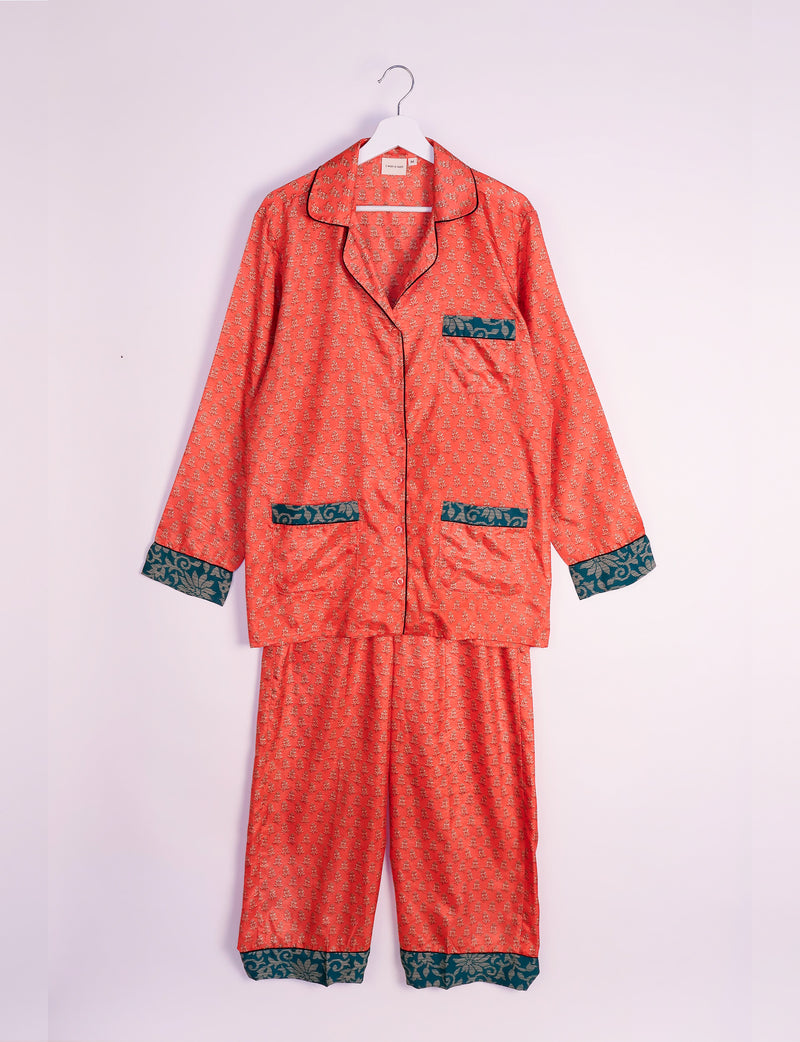 Orange long-sleeve pajama set with micro floral design and contrasting dark green patterned cuffs and pockets, hanging on a white hanger