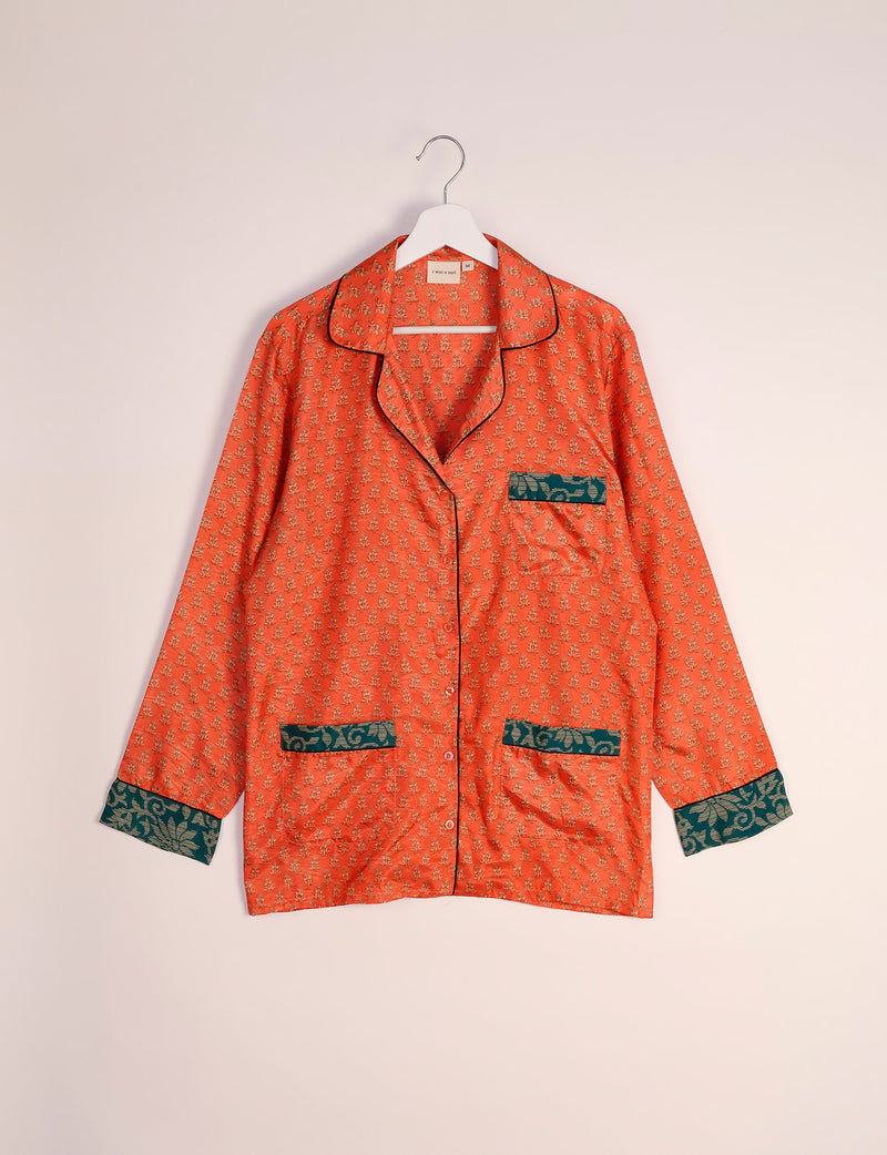 Orange long-sleeve pajama top with small floral print, dark green patterned cuffs and pockets, hanging on white hanger