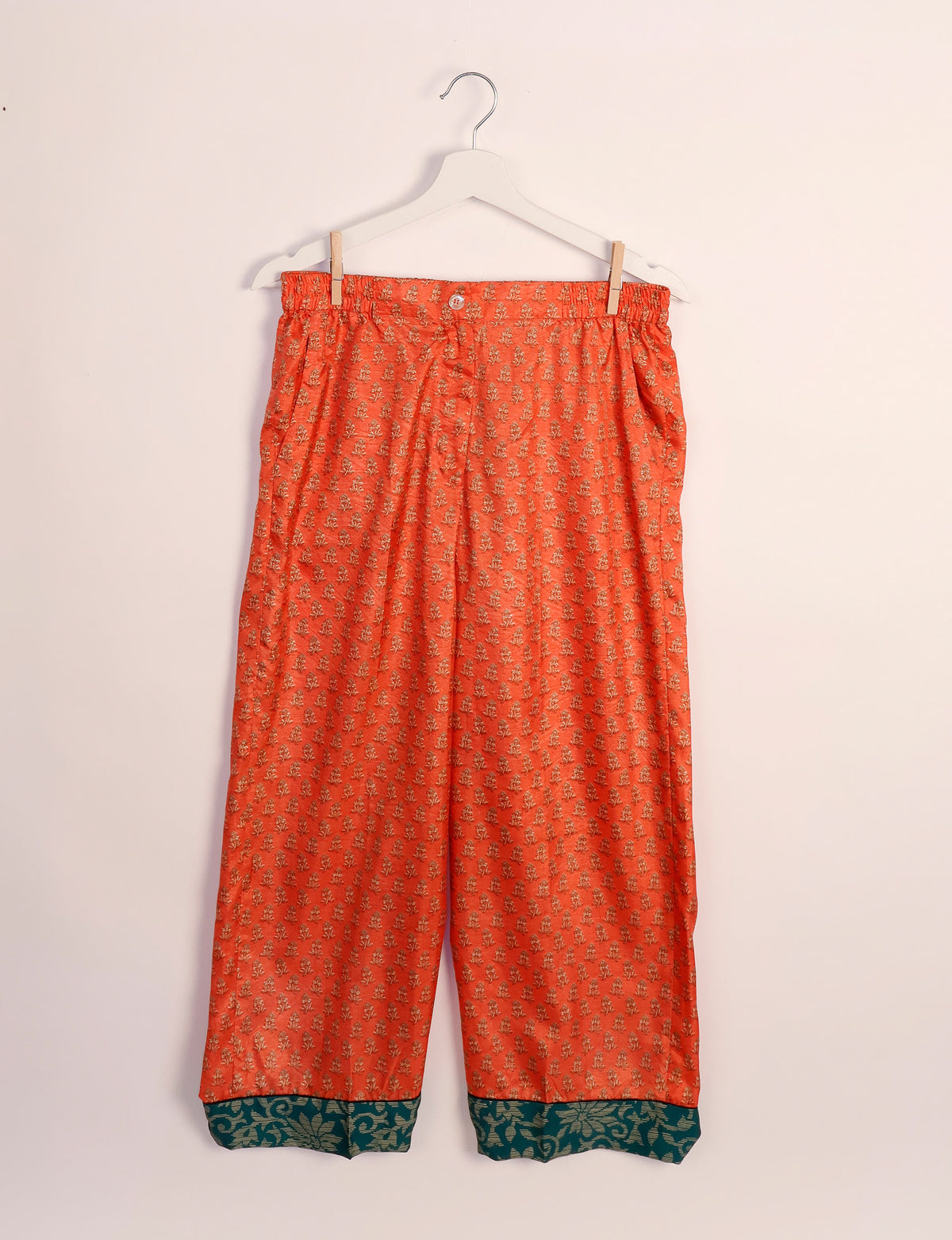 Orange pajama pants with small floral print and dark green floral patterned cuffs, hanging on white hanger front view