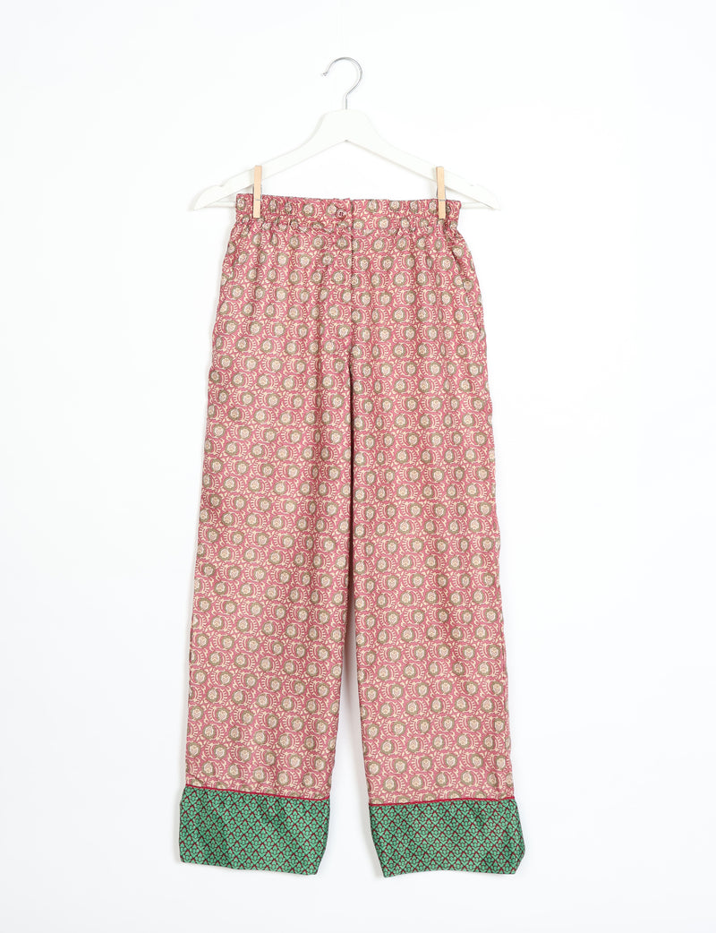 Pink patterned pajama pants with green patterned cuffs hanging on a white hanger against a white background
