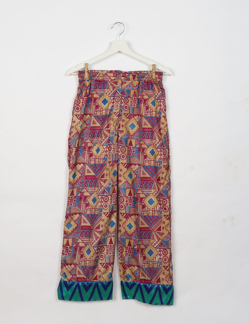 Pink geometric patterned pajama pants with blue and green zigzag cuffs hanging on a white hanger against a white background