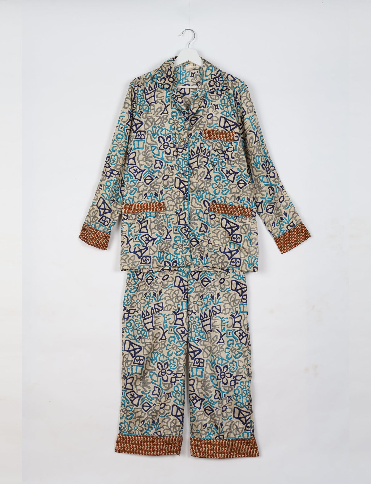 Beige long-sleeve pajama set with abstract blue and gray floral patterns, brown patterned cuffs, and front pockets, hanging flat