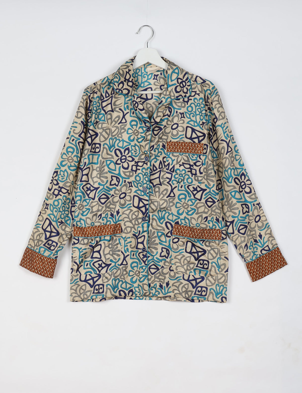 Beige long-sleeve pajama top with blue and gray abstract floral print, brown patterned cuffs and pocket trims, front buttons