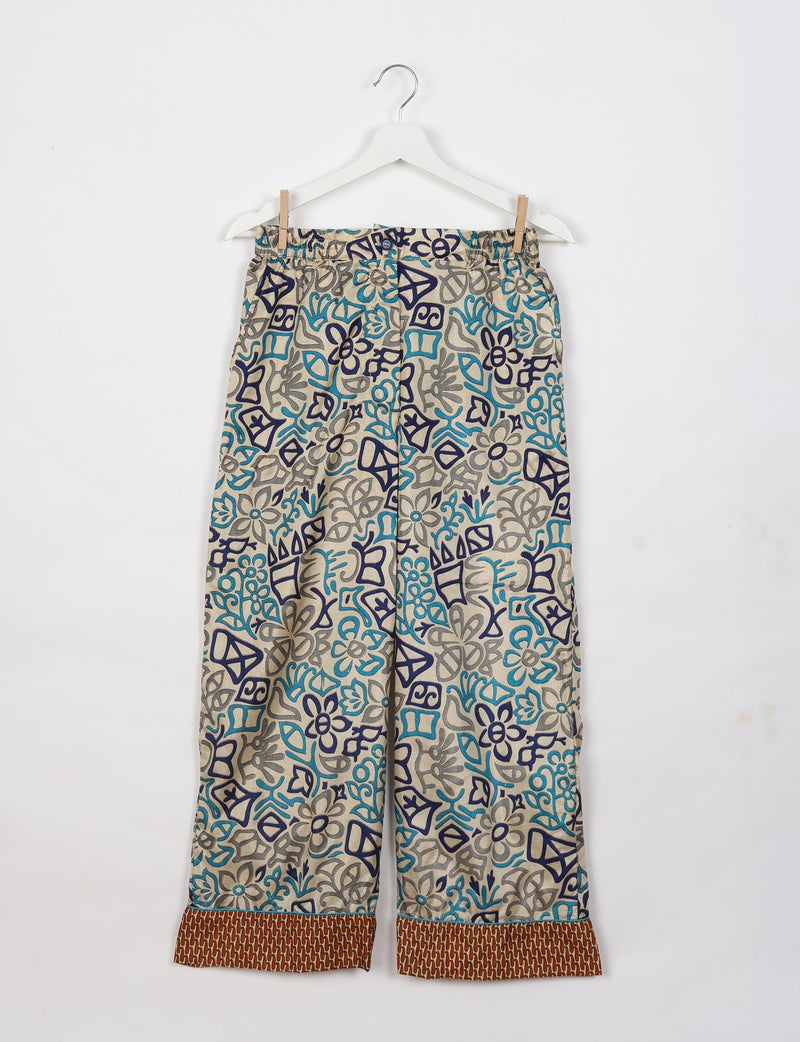 Beige pajama pants with blue and gray abstract floral print and brown patterned cuffs, hanging on white hanger
