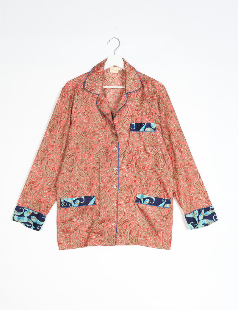 Long-sleeve orange paisley pajama top with blue paisley trim on cuffs and pockets, hanging on white hanger front view