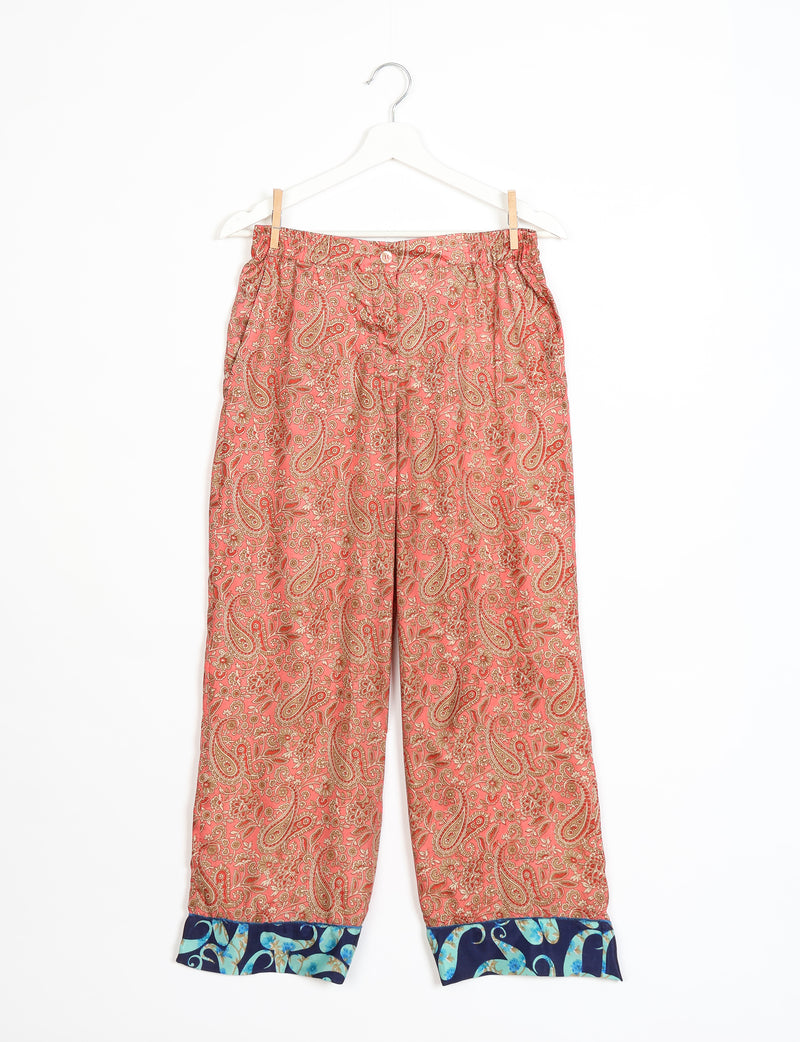 Orange paisley patterned pajama pants with blue floral cuffs, button and elastic waistband, hanging on white hanger