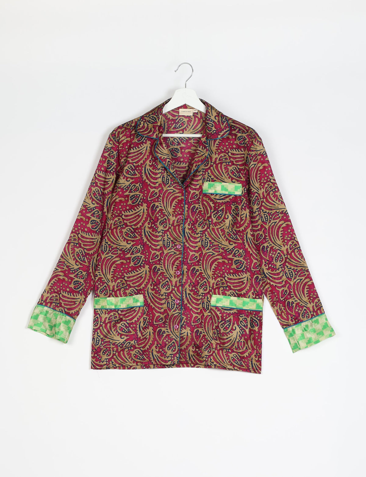 Long-sleeve red abstract patterned pajama top with green checkered cuffs and pocket trims, hanging on white hanger