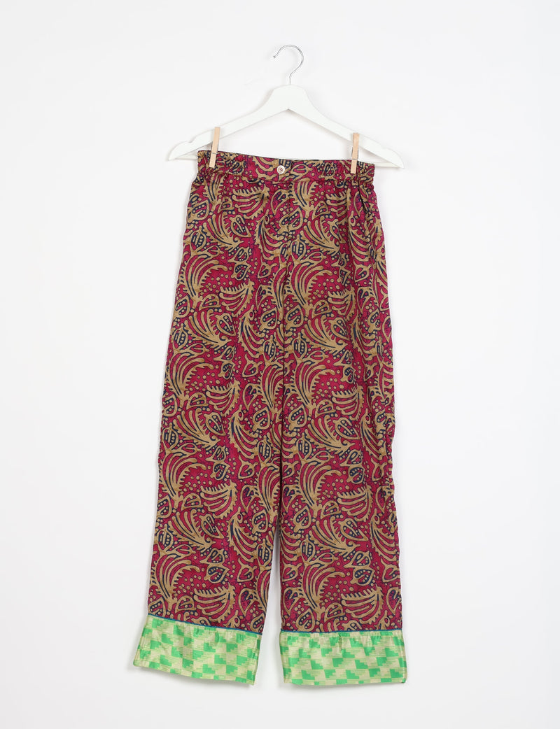 Red abstract patterned pajama pants with green checkered cuffs, button and elastic waistband, hanging on white hanger