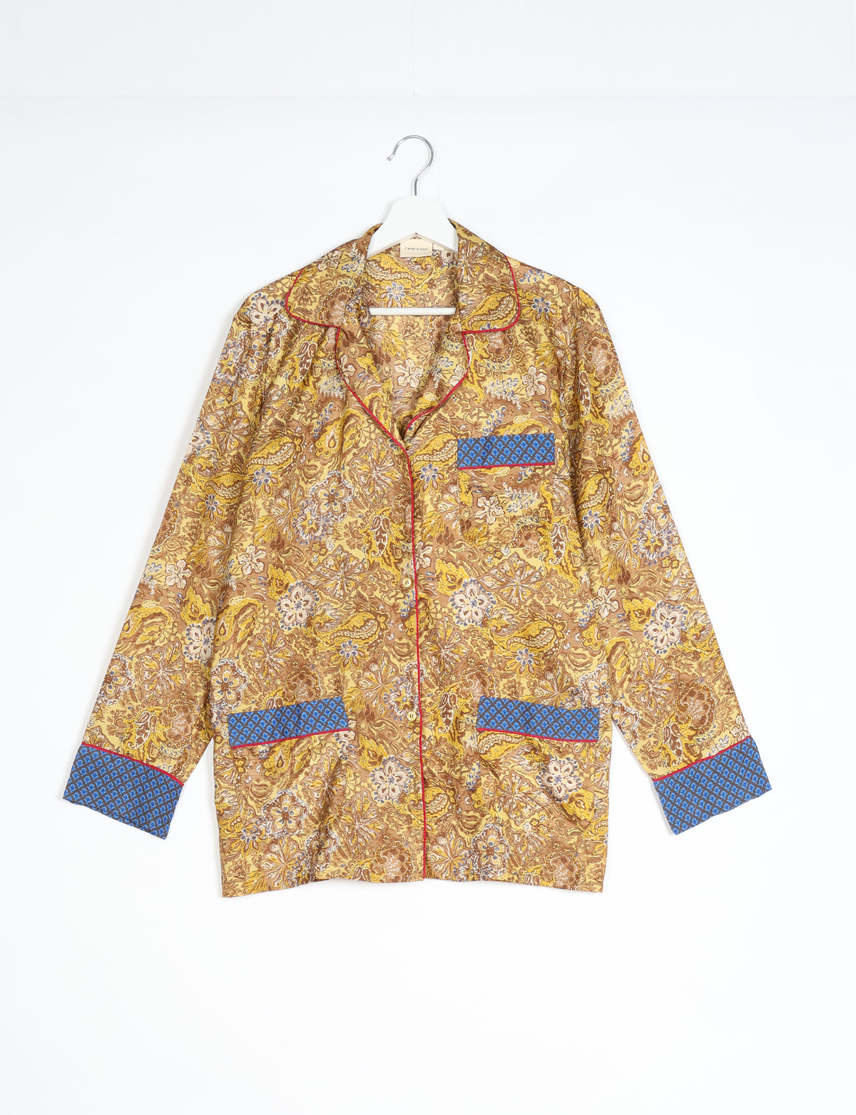 Yellow tropical print long-sleeve pajama top with blue patterned cuffs and pockets, red piping, hanging on white hanger