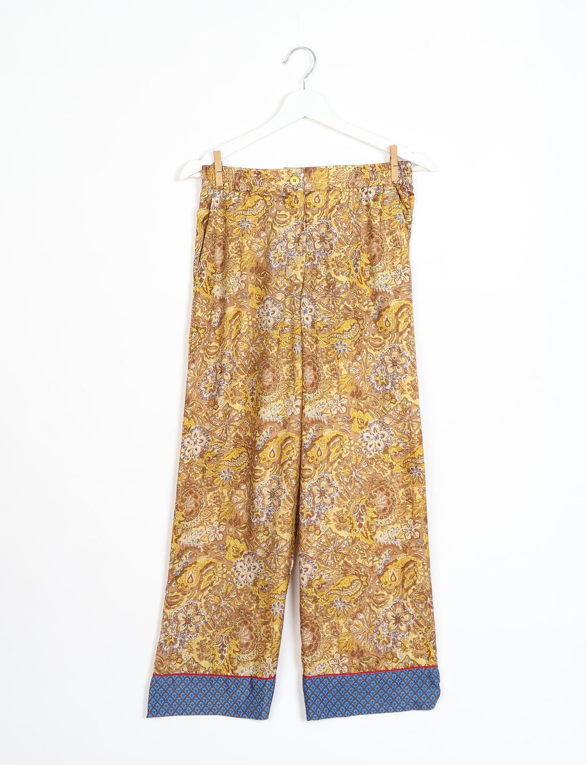 Yellow tropical print pajama pants with blue patterned cuffs, button closure, and elastic waistband hanging on white hanger