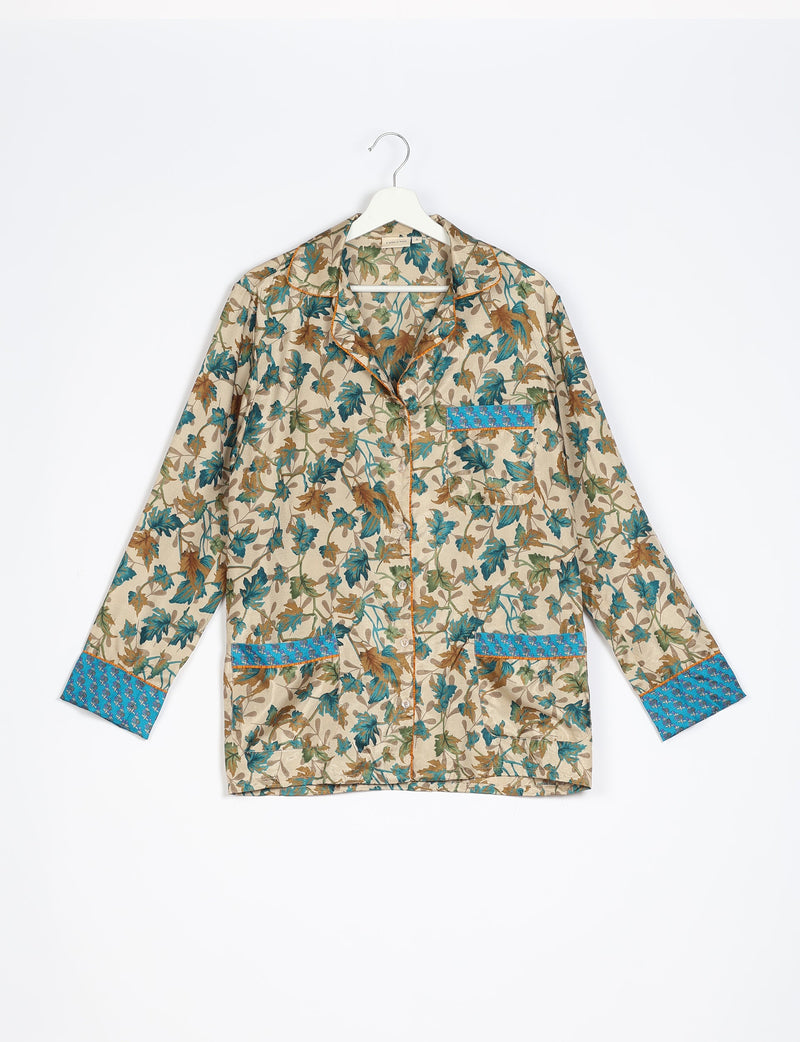 Beige long-sleeve pajama top with brown and teal leaf print, blue floral cuffs, collar, and pocket trim, hanging front view