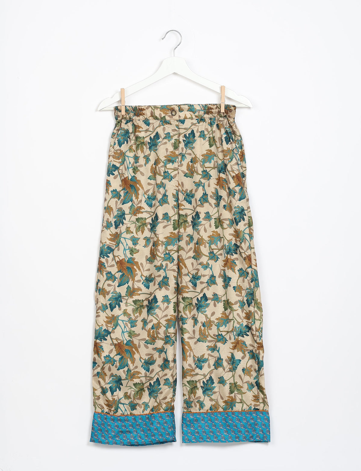 Beige pajama pants with long sleeves, featuring a blue and brown leaf pattern and blue cuffs with small floral print