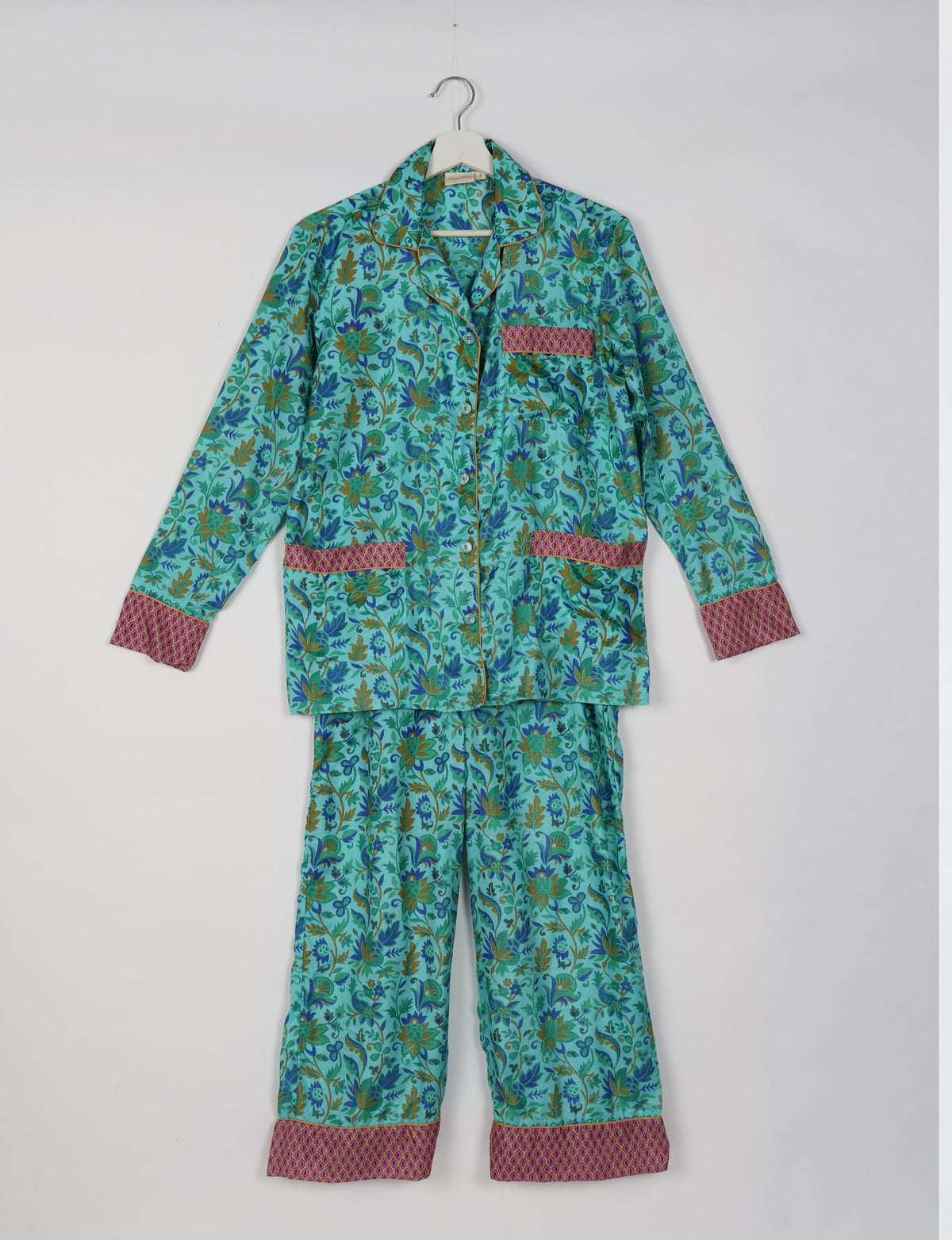 Blue tropical floral print long sleeve pajama set with pink patterned cuffs and pocket trim, hanging on white hanger