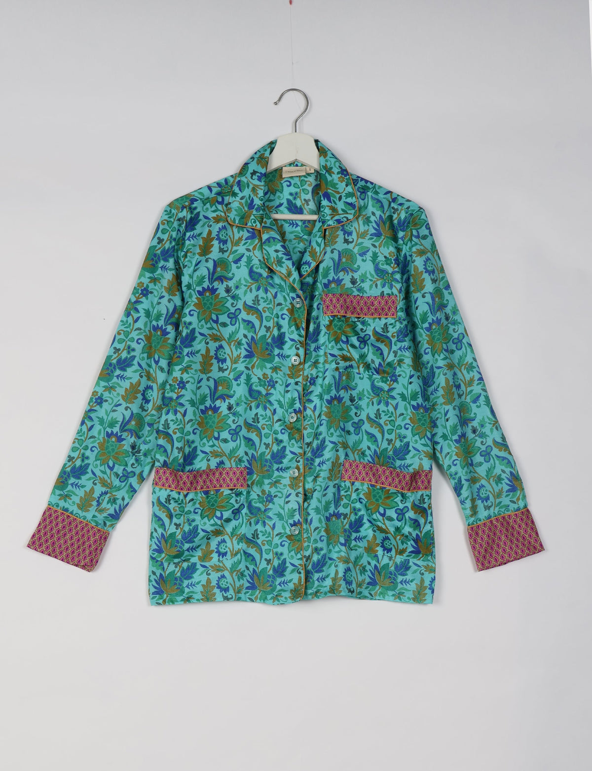 Blue tropical floral long-sleeve pajama top with pink patterned cuffs and pocket trim, hanging on white hanger front view