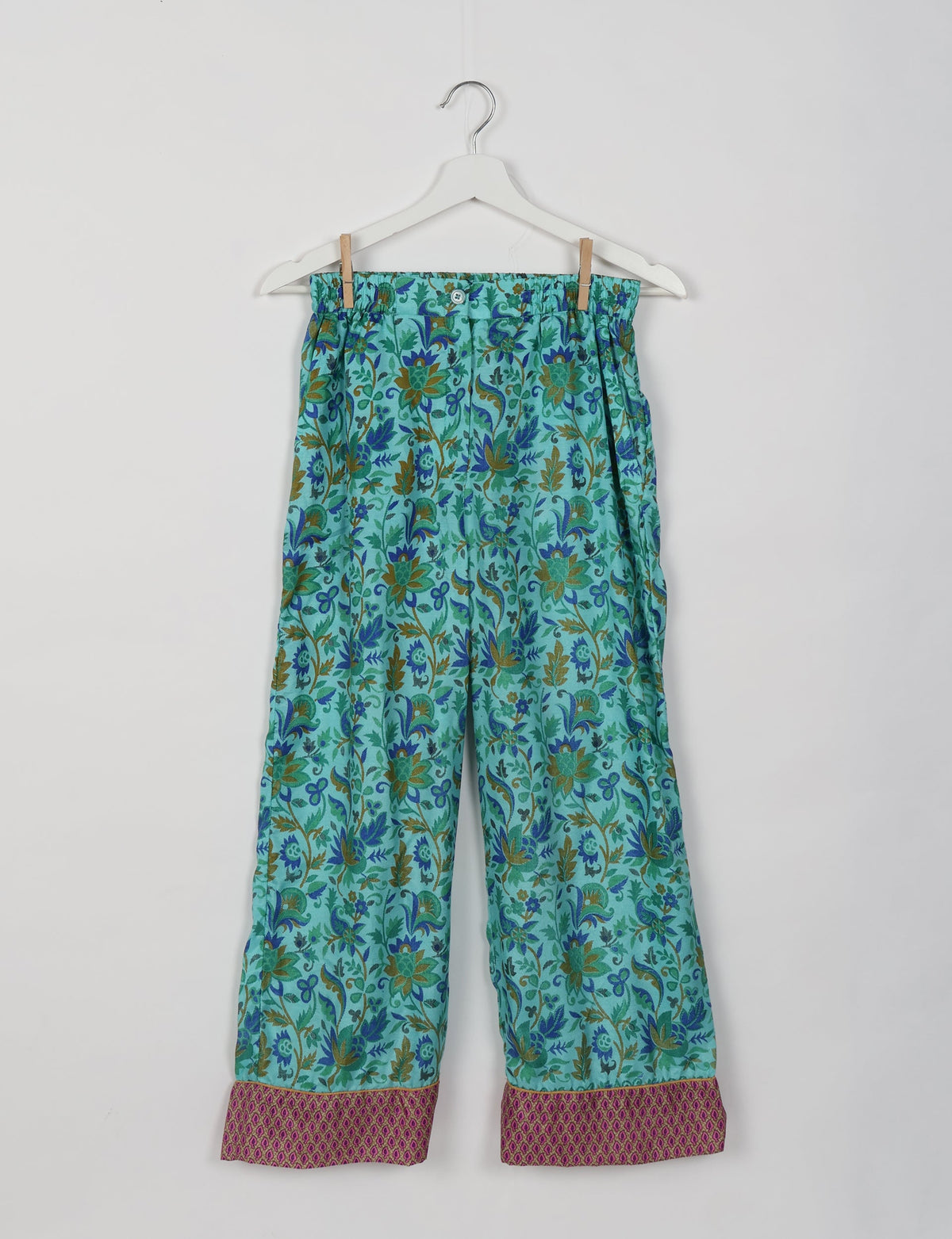 Blue tropical print pajama pants with elastic waistband and contrasting pink patterned cuffs, hanging on white hanger