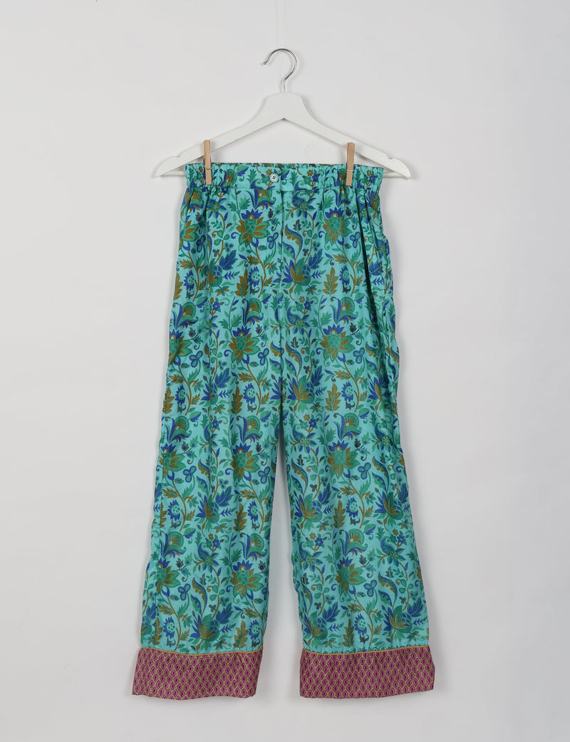 Blue tropical print pajama pants with elastic waistband and contrasting pink patterned cuffs, hanging on white hanger