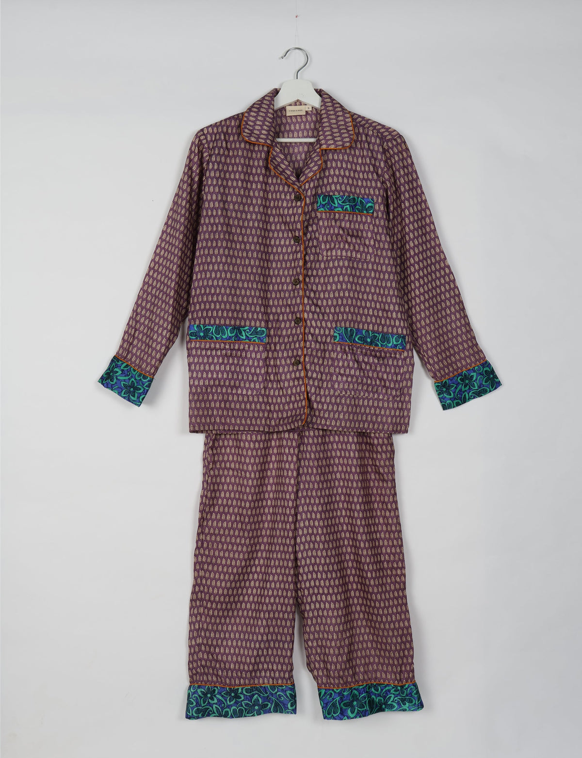 Purple pajama set with long sleeves and pants, featuring small beige leaf patterns and blue floral trim on cuffs and pockets