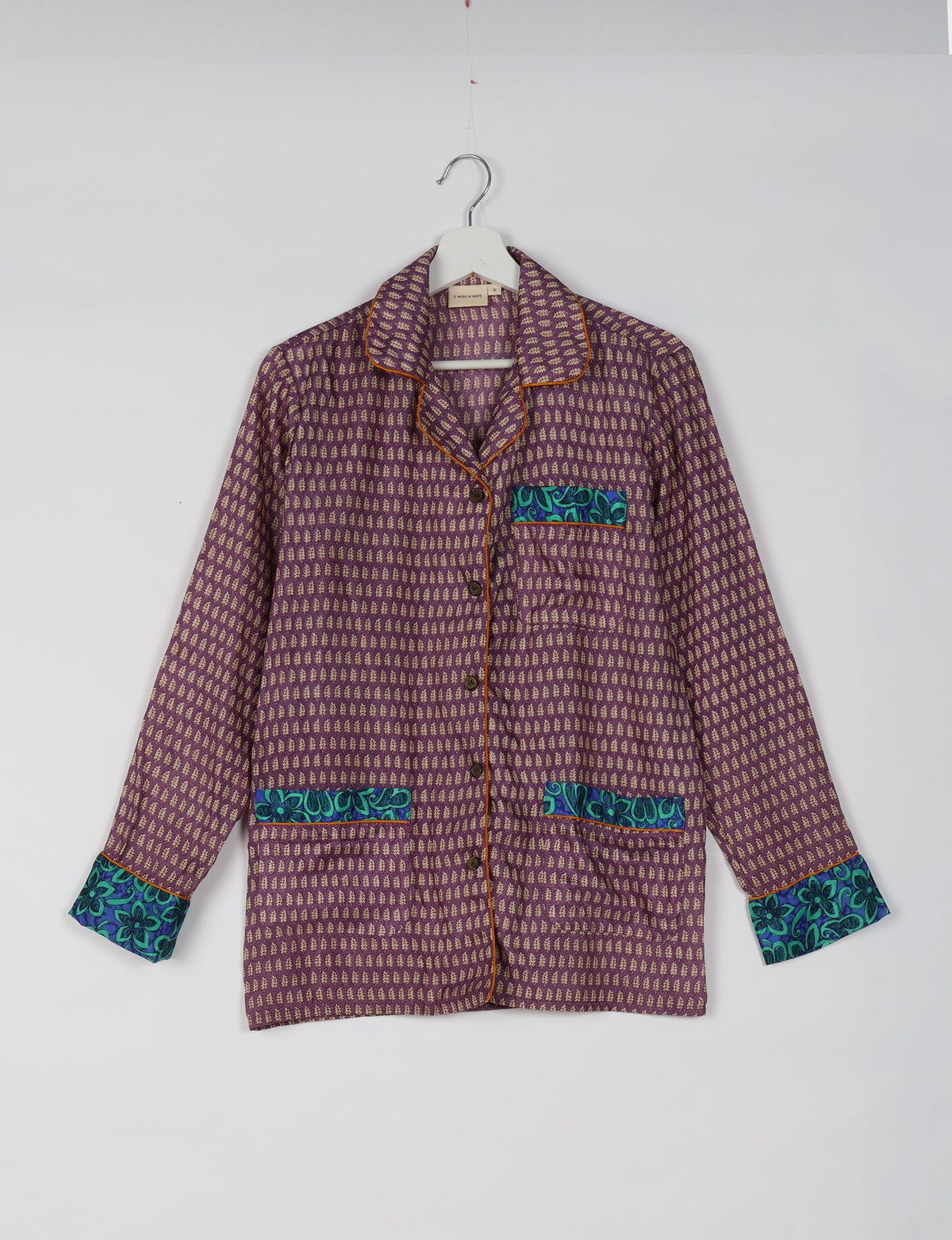 Purple long-sleeve pajama top with beige micro leaf pattern, blue floral pocket and cuff accents, and brown piping on hanger