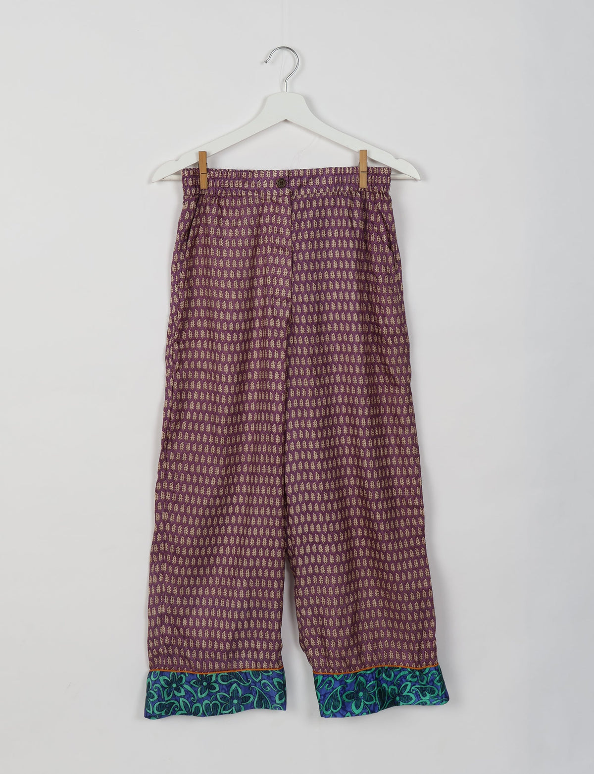 Purple patterned pants with blue floral cuffs hanging on a white hanger against a white background