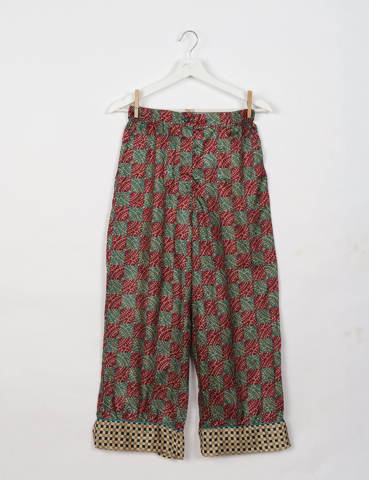 Red tropical patterned pajama pants with button and checkered cuffs, hanging on a white hanger