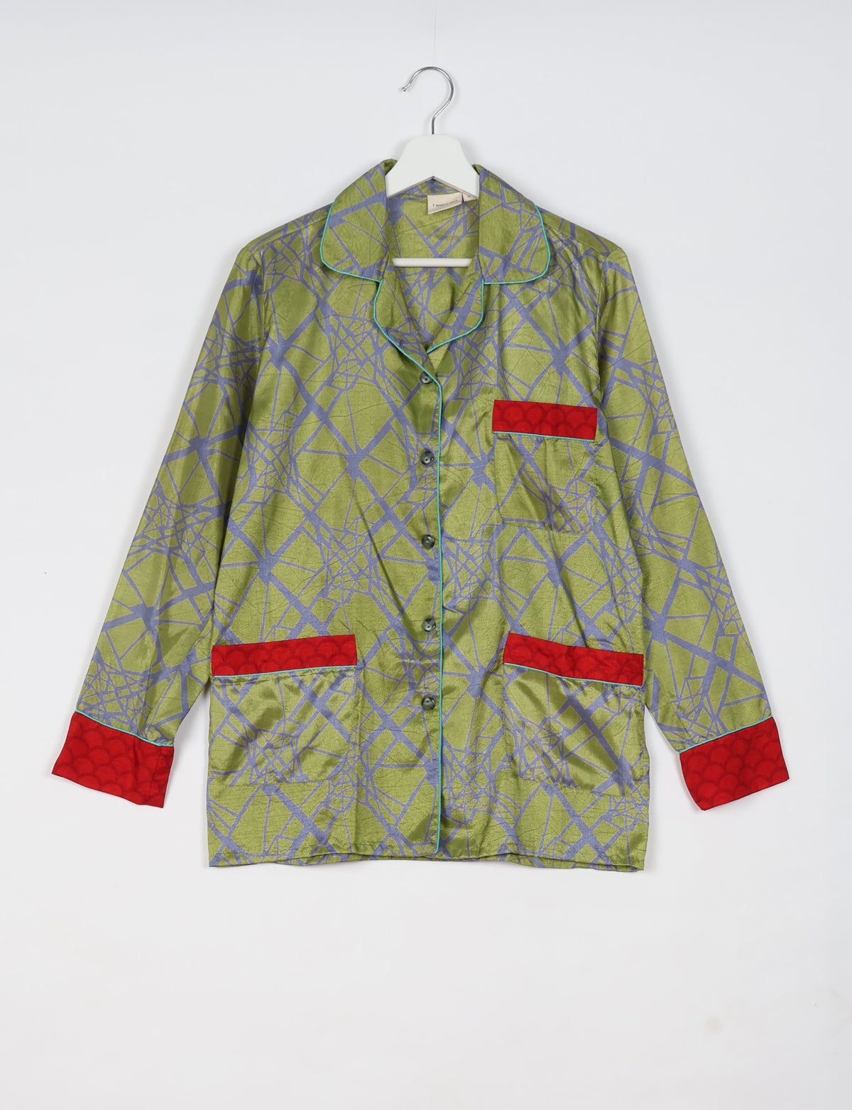 Long-sleeve green pajama top with abstract blue geometric pattern, red pocket and cuff accents, hanging on white hanger
