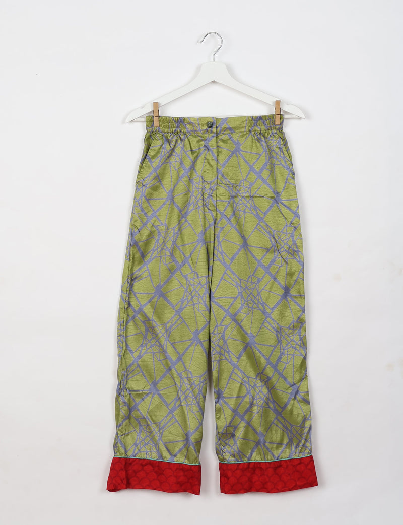 Green pajama pants with abstract gray geometric pattern and red cuffs, hanging on white hanger against white background