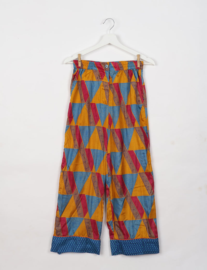 Yellow geometric patterned pajama pants with blue and red triangles and blue cuffed hems hanging on white hanger