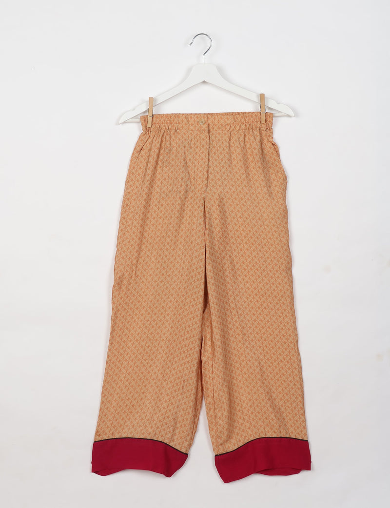 Beige pajama pants with micro circular pattern, elastic waistband, button closure, and red cuffs with black trim, hanging flat