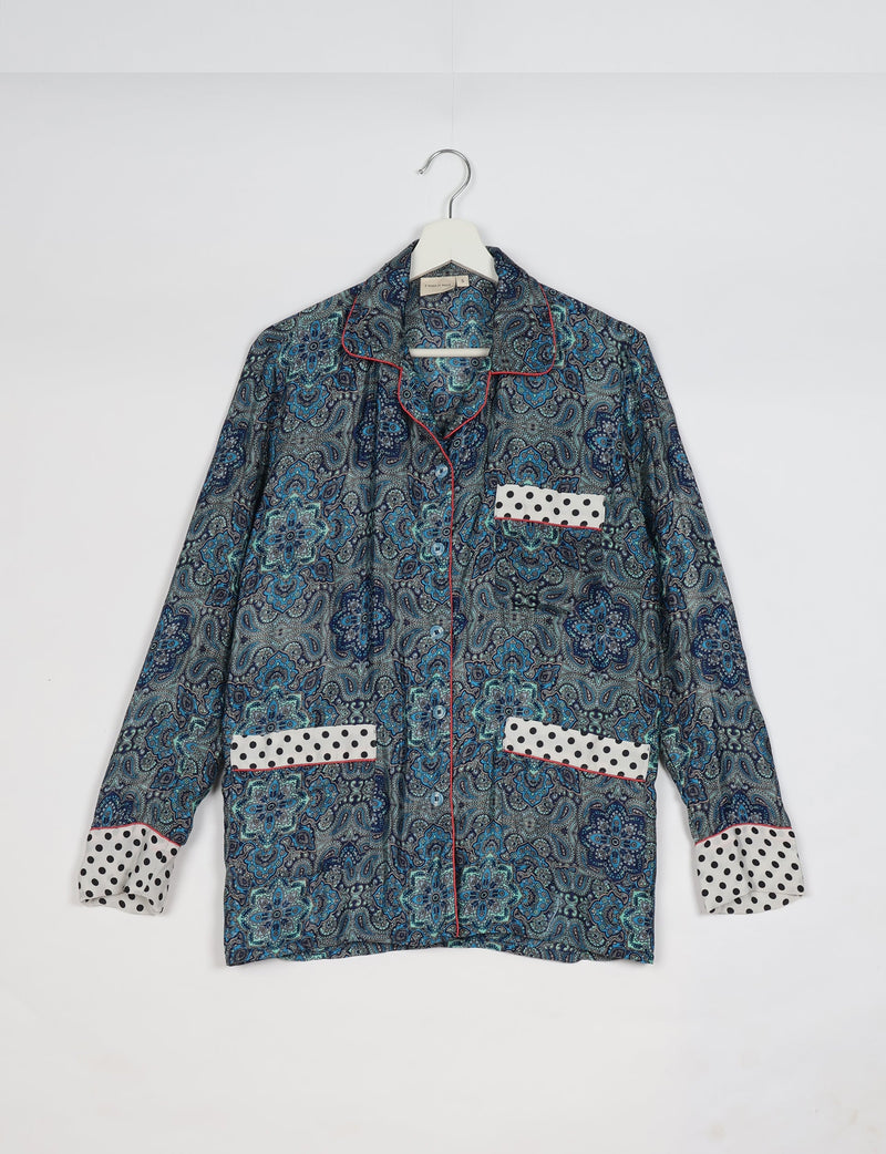 Long-sleeve button-up pajama top with blue paisley pattern, white polka dot pocket and cuff accents, red piping, on hanger