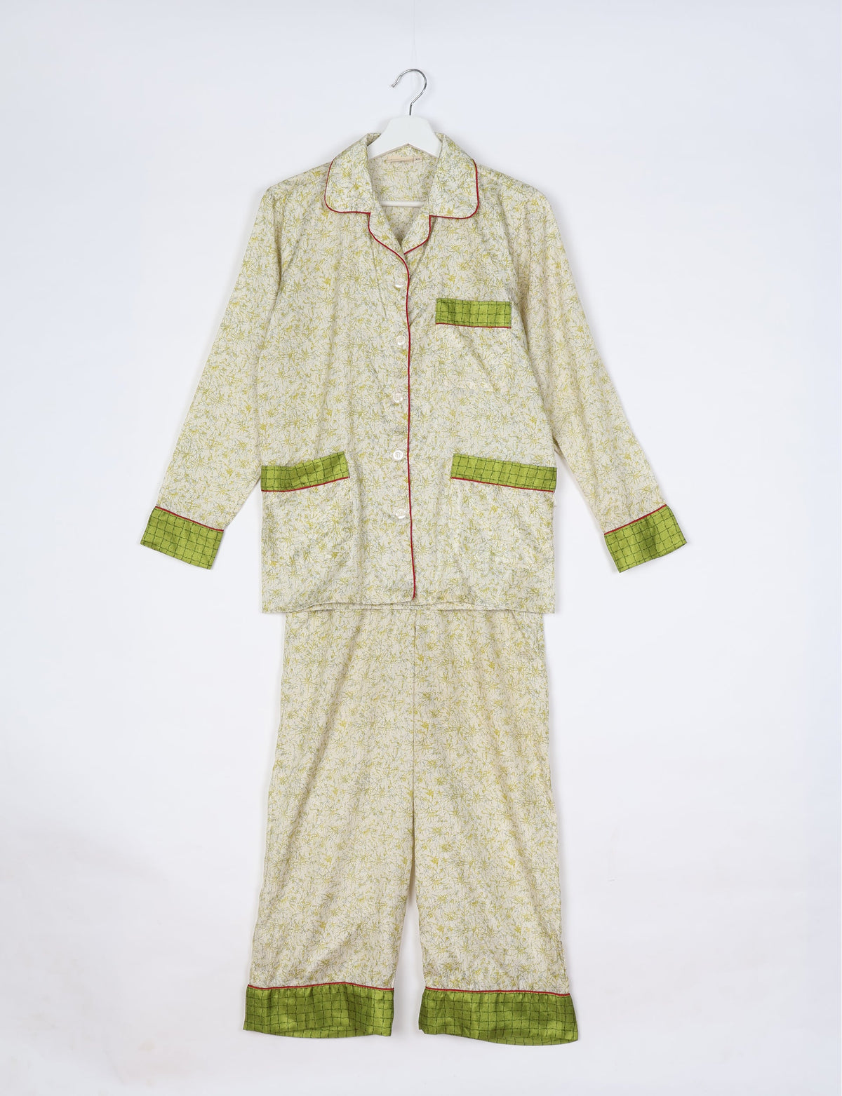 White tropical print long sleeve pajama set with green checkered cuffs, pocket trims, and red piping, hanging flat on hanger