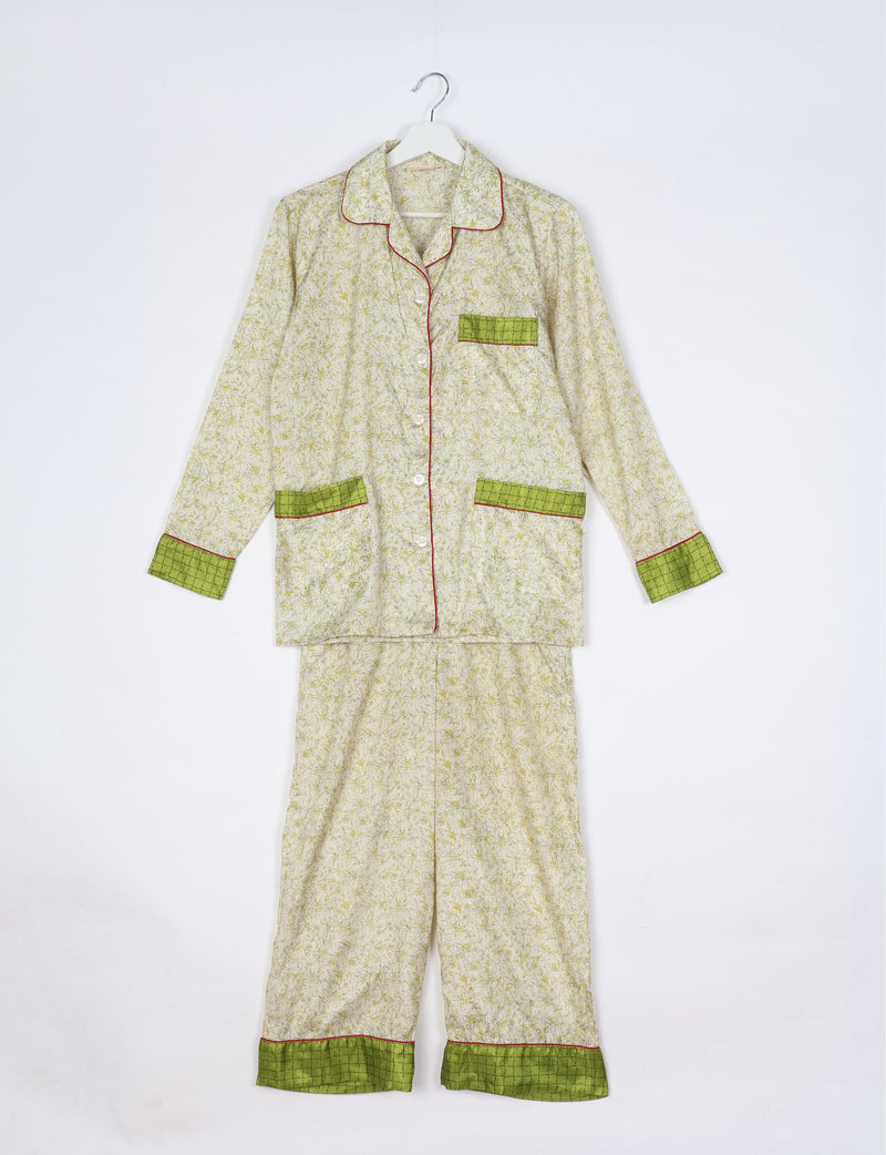 White tropical print long sleeve pajama set with green checkered cuffs, pocket trims, and red piping, hanging flat on hanger
