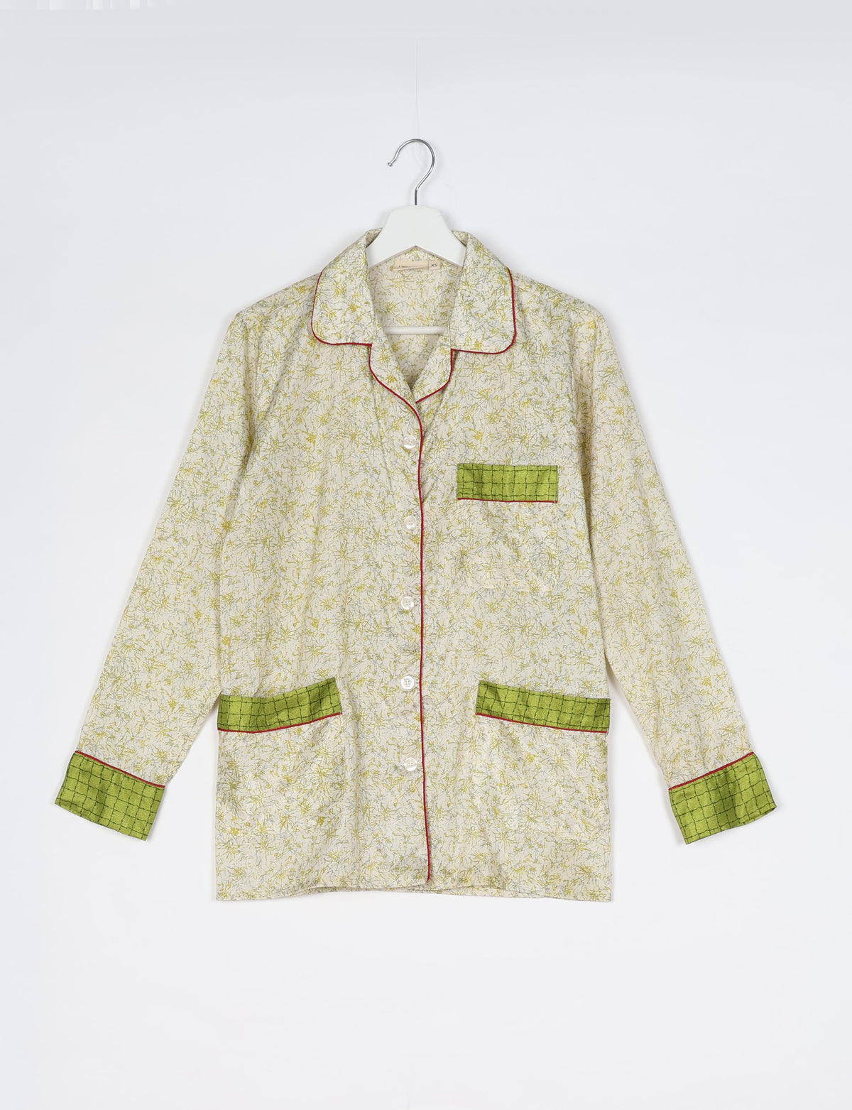Long-sleeve white pajama top with yellow tropical print, green checkered pockets and cuffs, red piping, button front, on hanger