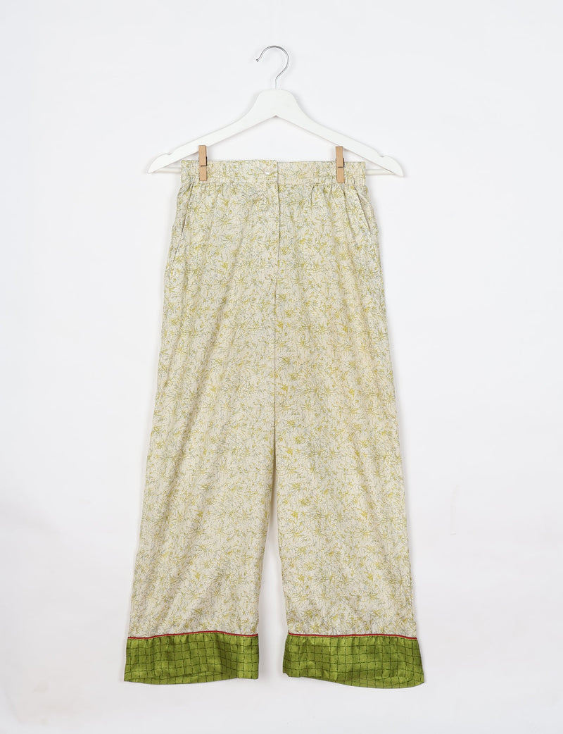 White pajama pants with yellow-green tropical print and green checkered cuffs with red trim, hanging on white hanger